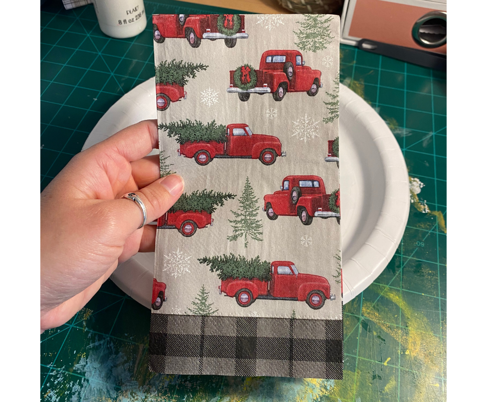 hand holding up Christmas napkin with red trucks on it
