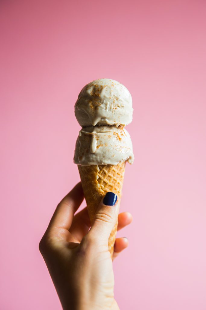 hand holding vanilla ice cream cone on pink background
